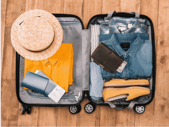 Open suitcase with hat, travel documents, yellow shirt, and electronic charger
