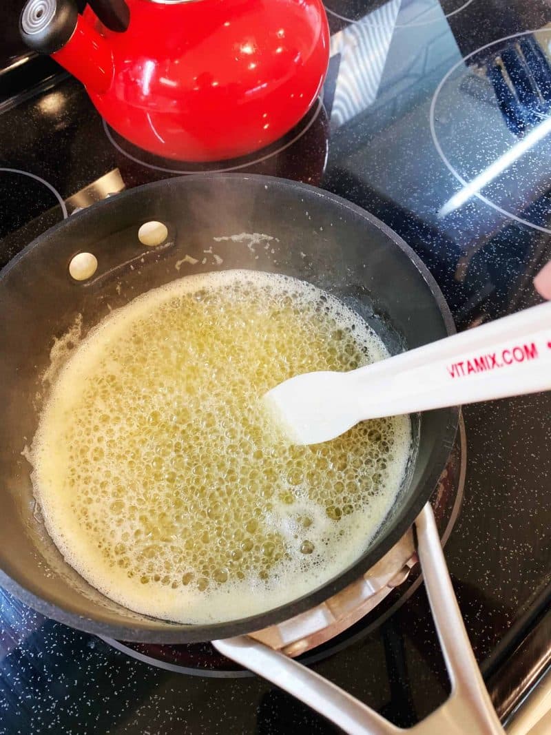 making glaze for a rum cake on the stovetop in a pot with a Vitamix spatula in the mixture and a red tea kettle on the side. 