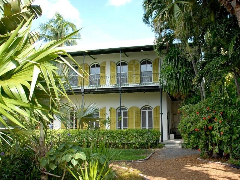 Ernest Hemingway's house in Key West. Yellow two story with expansive window and tropical greenery surrounding the house