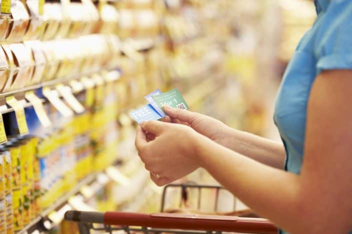 woman in grocery aisle using coupons to save money