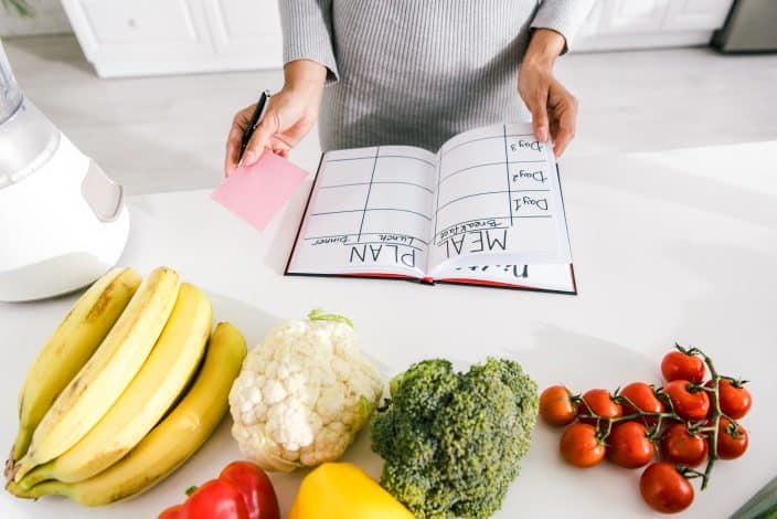 woman making a meal plan in notebook with a sticky note to help budget