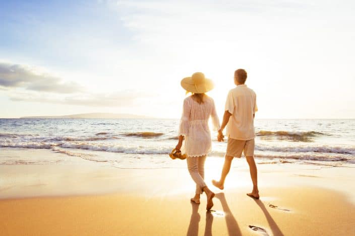 a couple walking on the beach with golden sand, bright sun and glistening waters. A perfect romantic getaway in the South