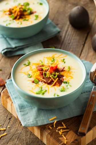 loaded cauliflower soup topped with bacon, green onions and cheese in a blue bowl on a wooden cutting board