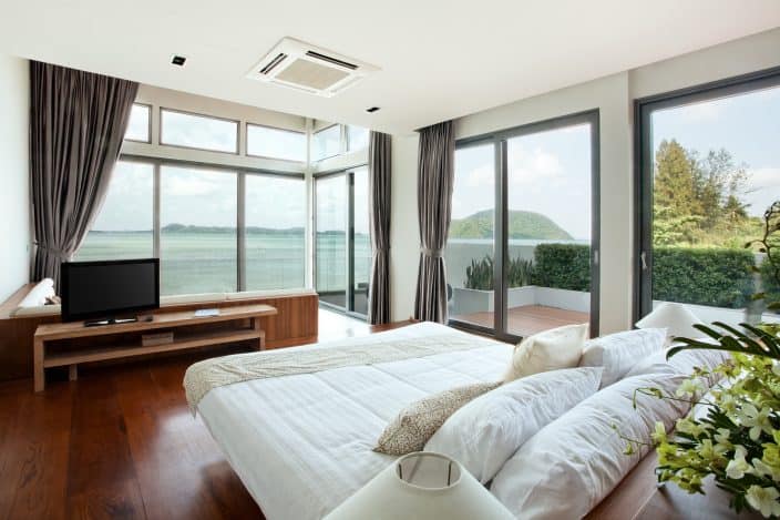 a hotel room with large windows greenery and wooden floors with a view of the water