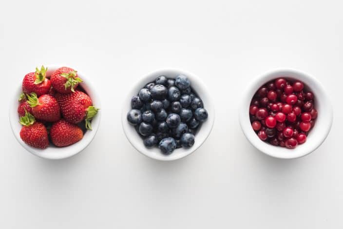 strawberries, blueberries, and cranberries in separate bowls to use as a topping for rice pudding