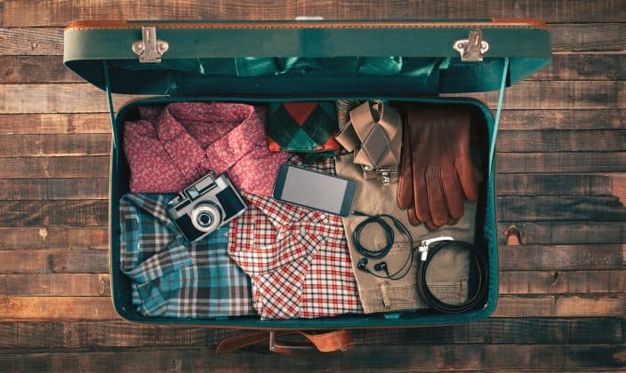 traveler packing, open suitcase on a wooden table with clothing, camera and mobile phone
