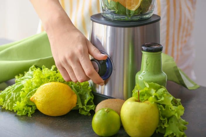 a woman preparing a green smoothie with apples, lemons, and greens