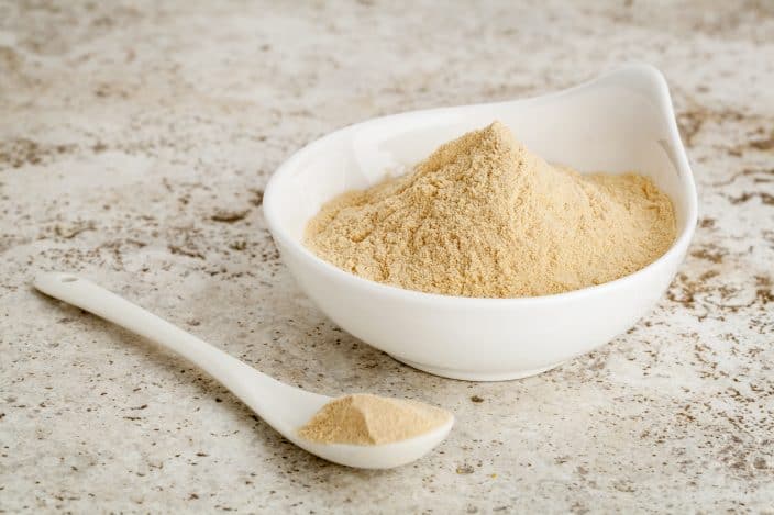 maca root powder a healthy addition for a smoothie - a small bowl with a spoon against ceramic tile surface