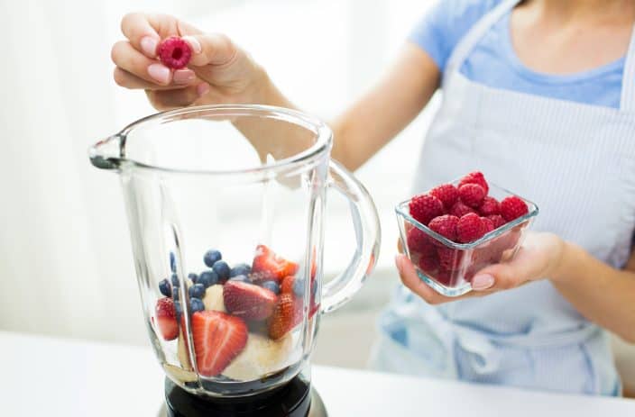 a woman putting berries into a blender to make a smoothie