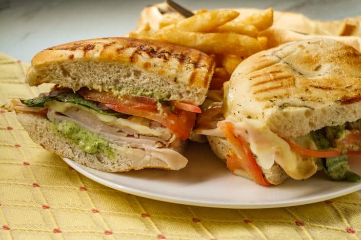 a finished turkey pesto sandwich cut in half on a plate with french fries