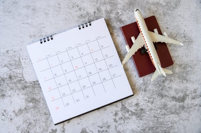 a calendar and toy airplane on top of a small red book on a concrete background