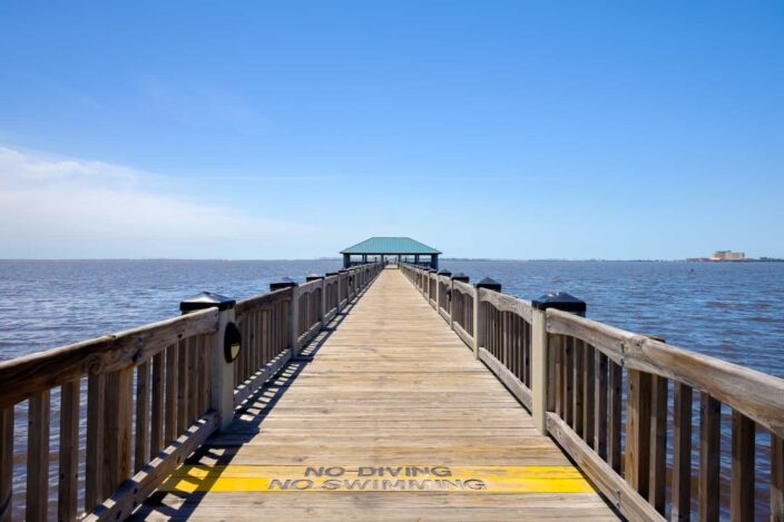 a pier with the words no swimming or diving on it over water in Ocean Springs, Mississippi, with blue skies and dark blue waters 