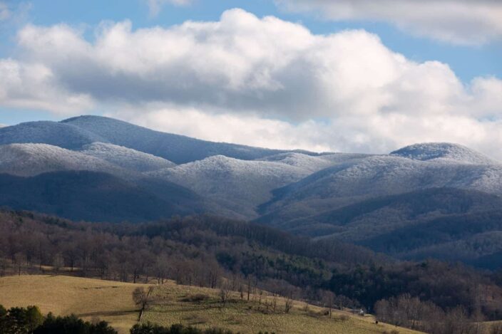 Picture of the Appalachian mountains in the daytime with ice on the mountains and clouds and brown leafless trees in one frame.