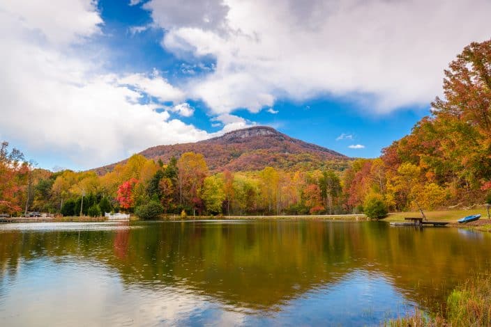 a lake in Georgia with a surrounding mountain with fall foliage, blue skies, and a boat and dock on the side 