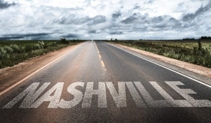 Nashville sign on printed on the clear road with grey skies, clouds, and grass on either side of the road