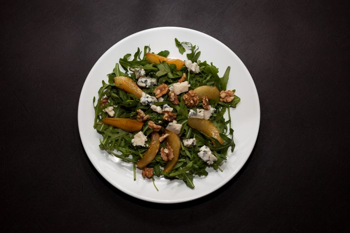 Pear and Blue cheese salad with Arugula, warm caramelized pear, walnuts and blue cheese. Top view, dark background