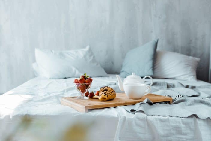 a bed with grey walls and a breakfast platter sitting on the bed to represent a bed and breakfast for travel deals