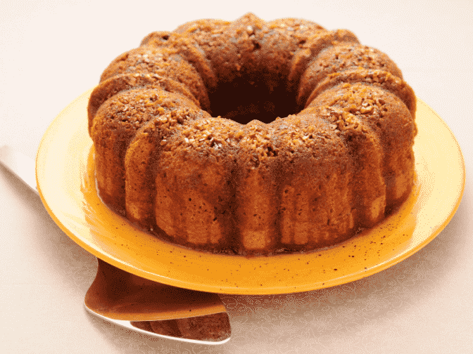 A Caribbean rum cake on a yellow plate on a beige counter top with a silver spatula 