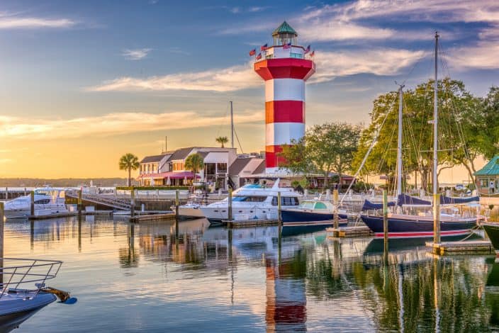 lighthouse with red and white stripes on the  water with boats tied up
