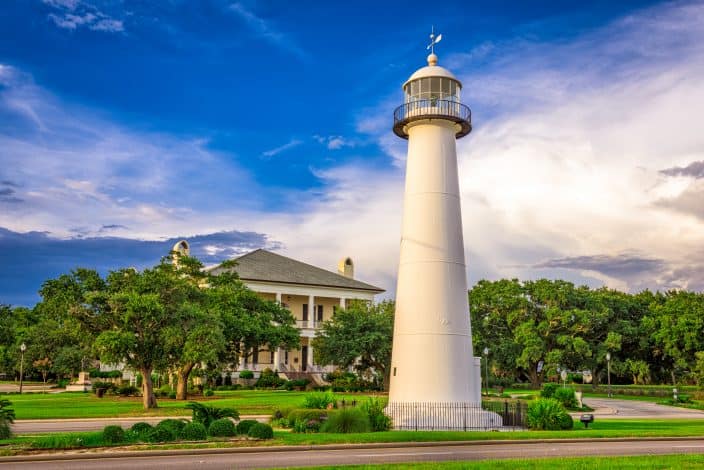 Biloxi, Mississippi USA at Biloxi Lighthouse, with blue skies, green trees and grass, and a yellow mansion in the background, an example of romantic getaways for the weekend