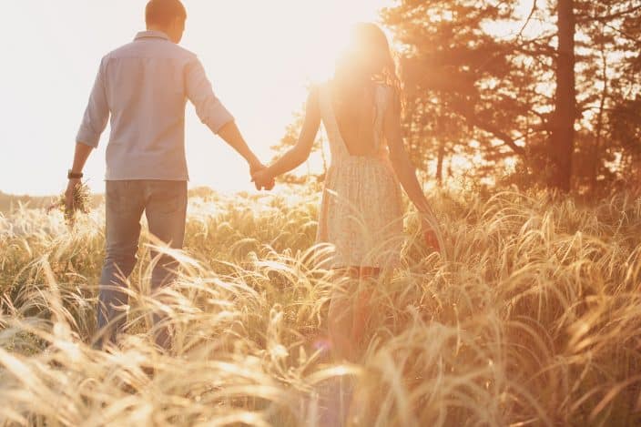 a couple walking in a tall grass field with the sun shining a representation of romantic getaways for the weekend 