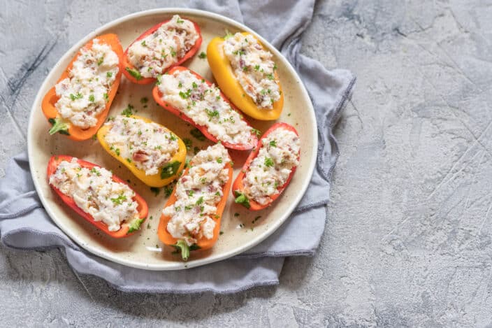 cheese stuffed mini peppers with bacon and herbs on a plate before broiling