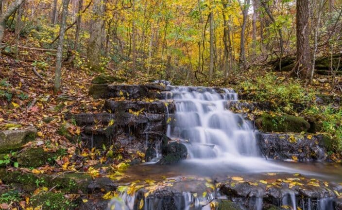 The Ozark mountains with a small waterfall and autumn leaves on the trees, an example of where to stay during your romantic getaway arkansas