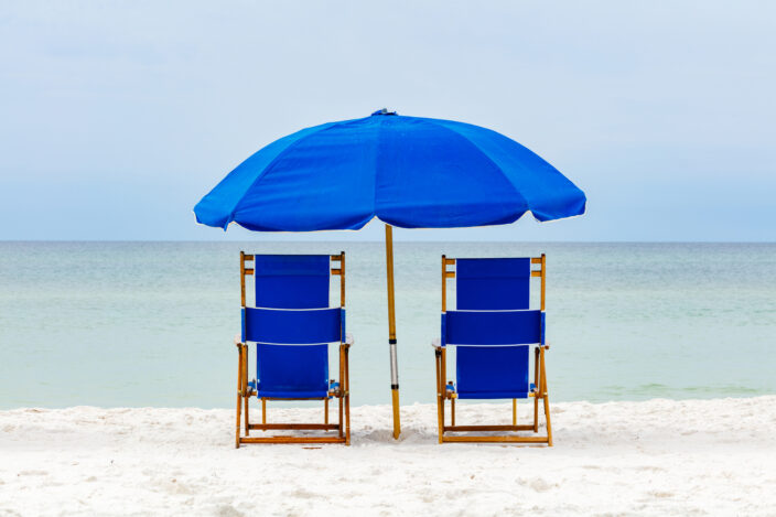 blue beach chairs on white sand facing the light turquoise water of the Gulf of Mexico