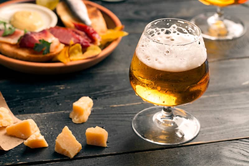 Two glasses of beer on black table with snacks