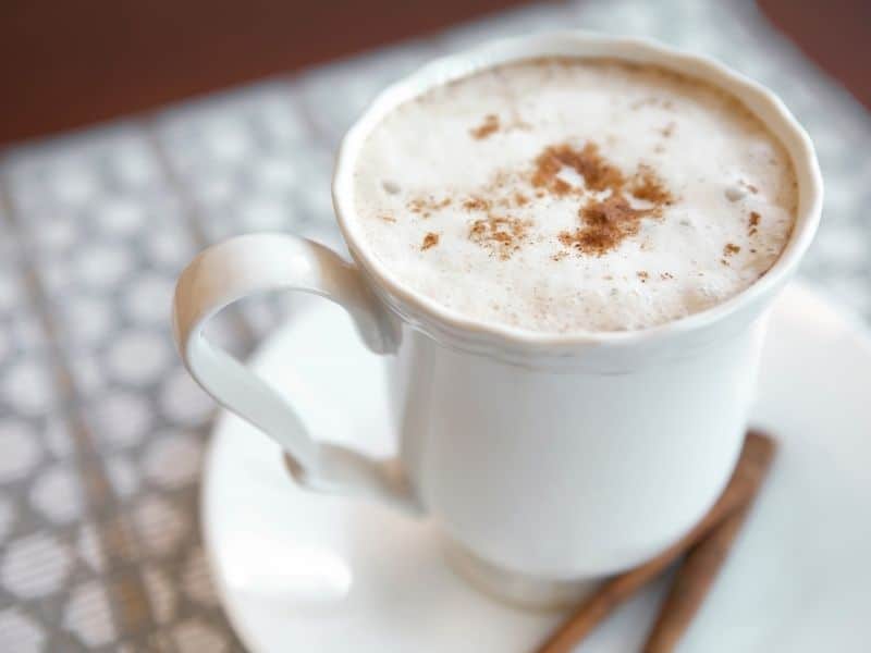 a pumpkin spice latte in a white mug with cinnamon sticks on a white placemat, an example of pumpkin healthy recipes