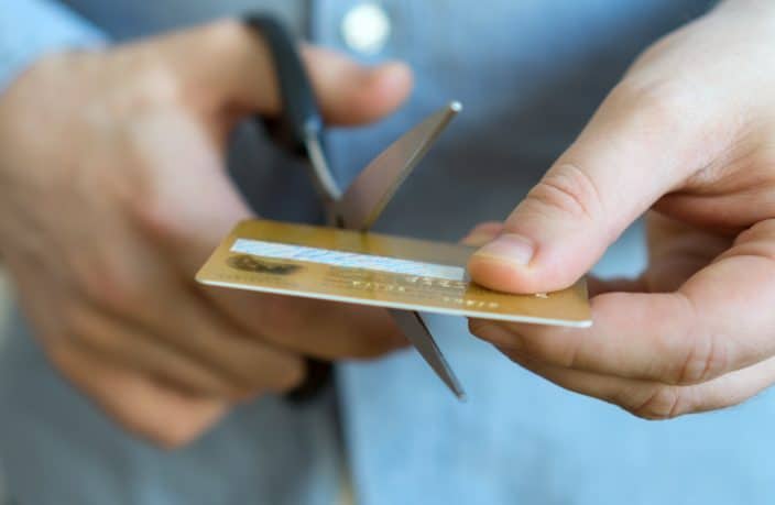 a male hand cutting up a credit card as a symbol of stopping credit card use to lower debt