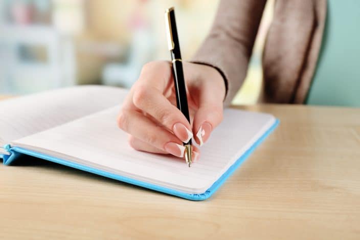 a female hand writes in a notebook on a table to make a list of her debts