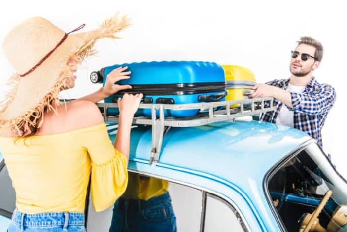 A man and woman strapping down packed suitcases on top of their car for travel 