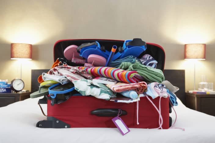 Travel essentials messily stuffed into an overpacked red suitcase on a bed