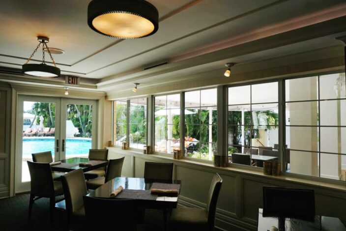 The inside dining area at The Secret Garden with a view of the pool with dark wooden tables, fabric chairs, low, ambient lighting 