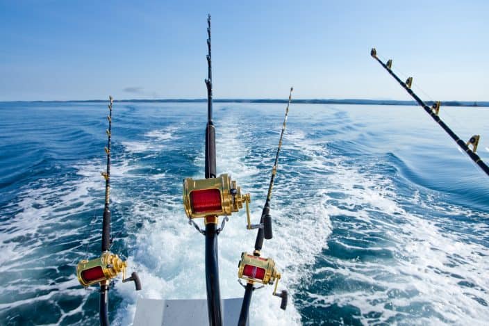 the of 4 deep sea fishing poles cast off the back of a fishing boat with blue water in the background and bright blue skies