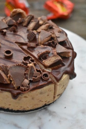 view of Reese's peanut butter cheesecake from the top with chunks of peanut butter cup on chocolate ganache frosting