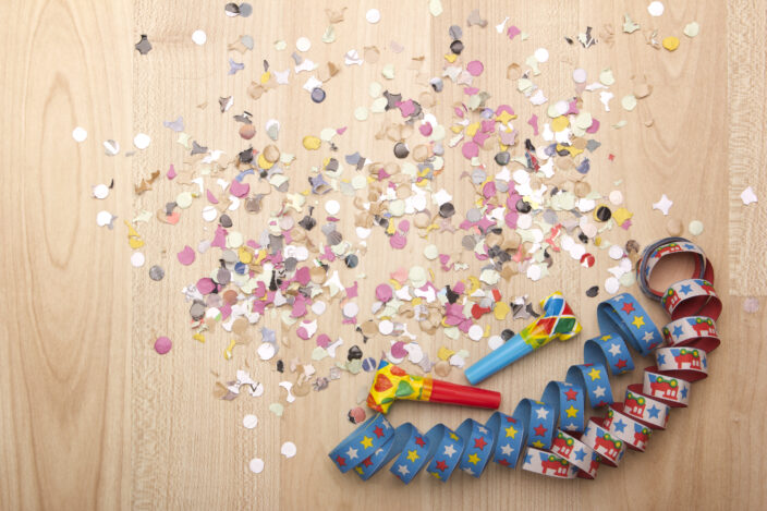 confetti and noise makers on a tan block are essential for Celebrating New Year's Eve at home