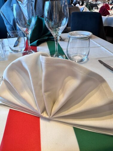 On the MSC Seaside white tablecloth on table, glasses, wine glasses, white plates and silverware, with a red, white, and green strip table runner