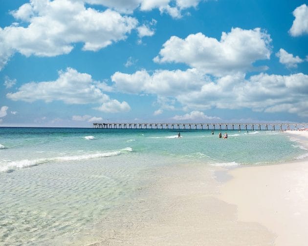 Turquoise water, bordered by a long fishing pier perched on a white sand beach