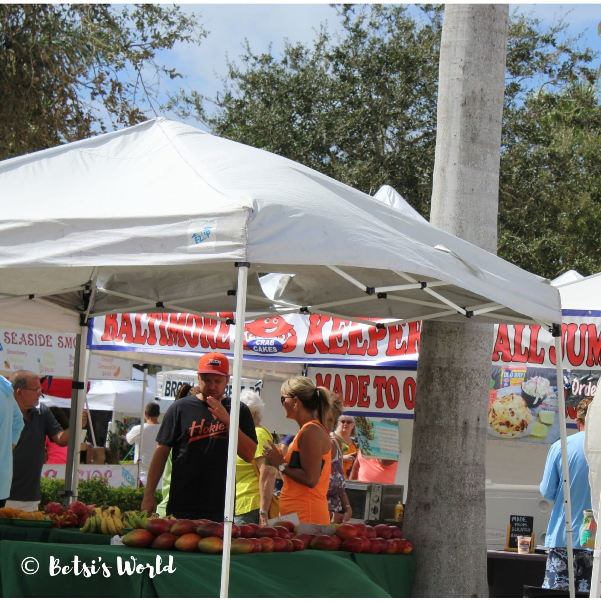A fresh produce stand at Fort Pierce's Farmers' Market with mangos and people talking, blue skies and palm trees