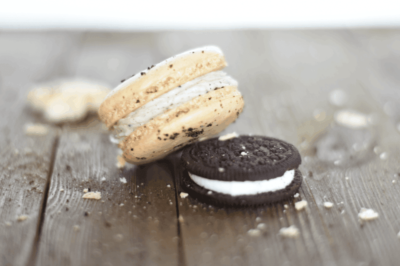 Oreo macaroon and an oreo cookie on a wood plank table with crumbs