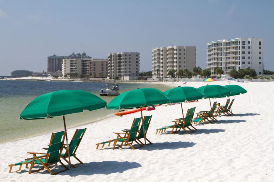 Tourists relax laying on the beach behind beach umbrellas and beach chairs with highrise condominiums in the background.