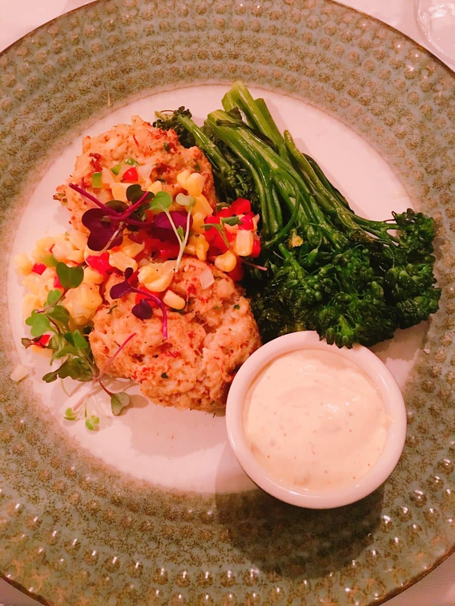 crab cakes topped with salsa, broccolini and sauce plated on a white and gold green plate at a restaurant in St. Simons Island, a romantic beach getaway destination