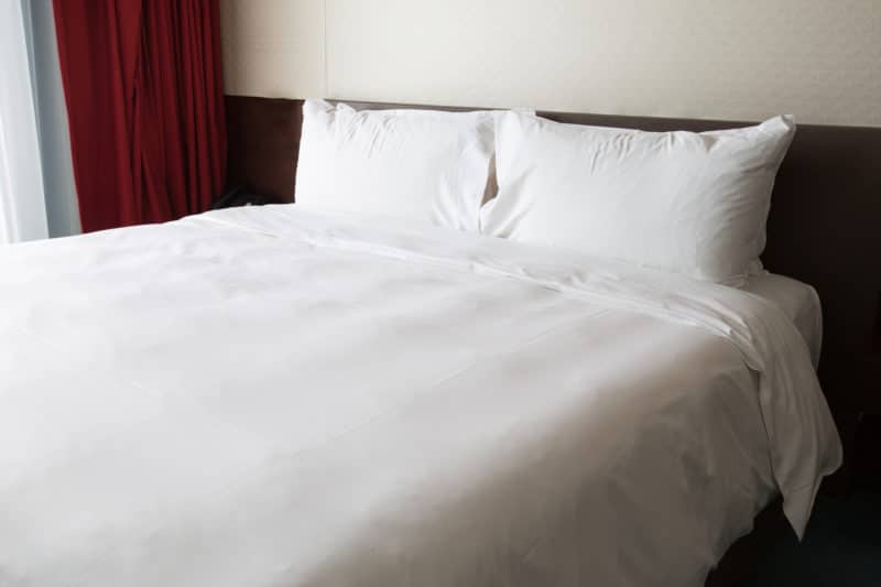 white sheets, 2 pillows, dark headboard