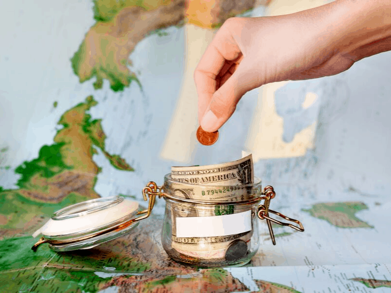 money jar with coins laying on world map