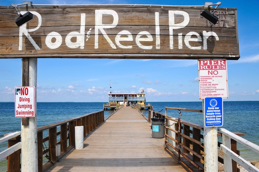 Rod and Reel Pier sign on a boardwalk in the ocean with blue skis. This is a great spot for some dinner on your vacation.