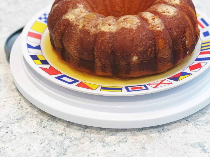 Rum cake out of pan and on a plate decorated with nautical flags and rum glaze pooling around sides and in middle
