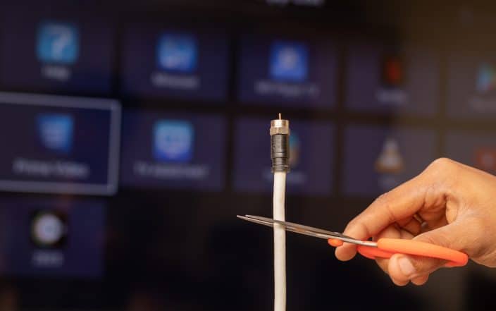 male cutting a cable cord in front of a screen with streaming services to help save money