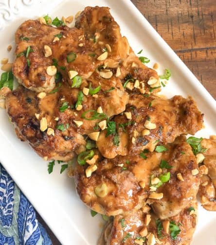 Thai Chicken Thighs on white platter garnished with green onion and chopped peanuts.